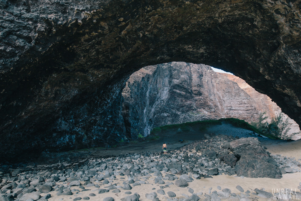 A person walks under the enormous arch at Honopu Beach, Kauai, Hawaii